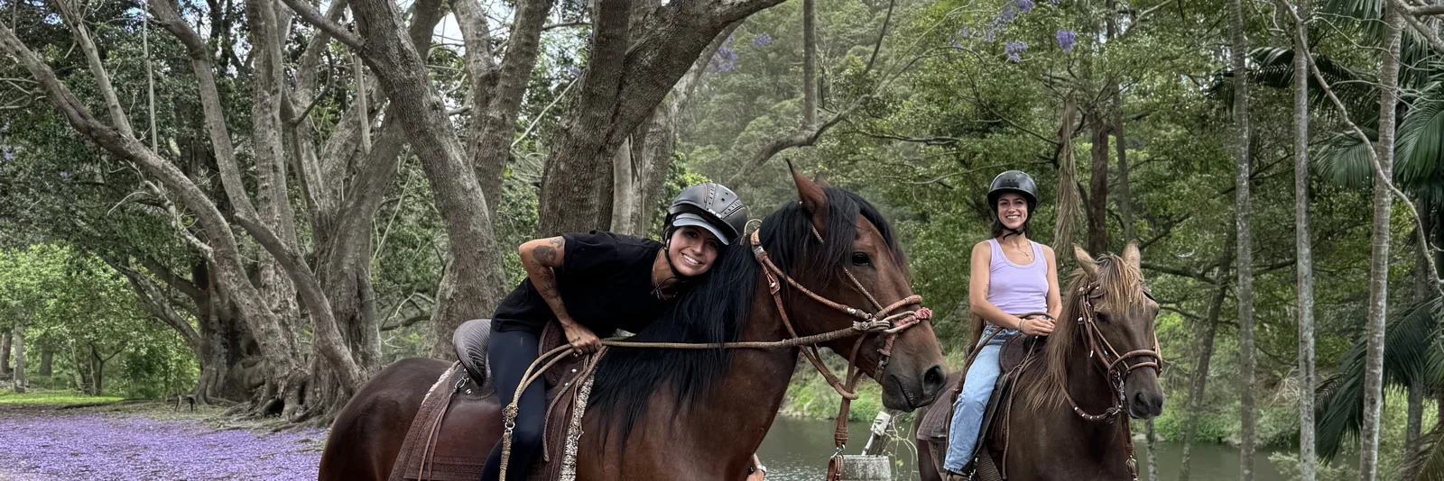 Two riders on horseback beneath the jacarandas beside the river at Historic Rivermill